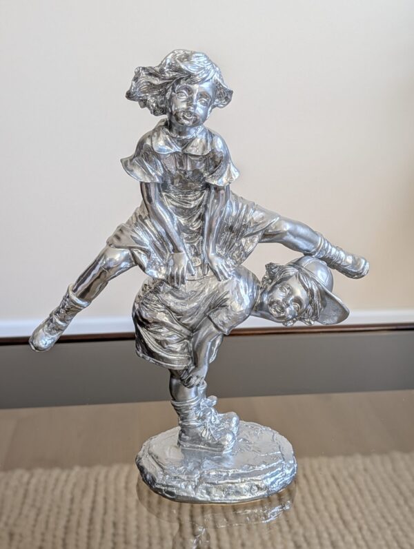 Statuette en plâtre "enfants jouant à saute-mouton" fabriquée entre 1950 et 1980. Son sujet de style dit "classique" et sa modernisation avec une peinture chromée en font une pièce hors catégorie et remarquable.